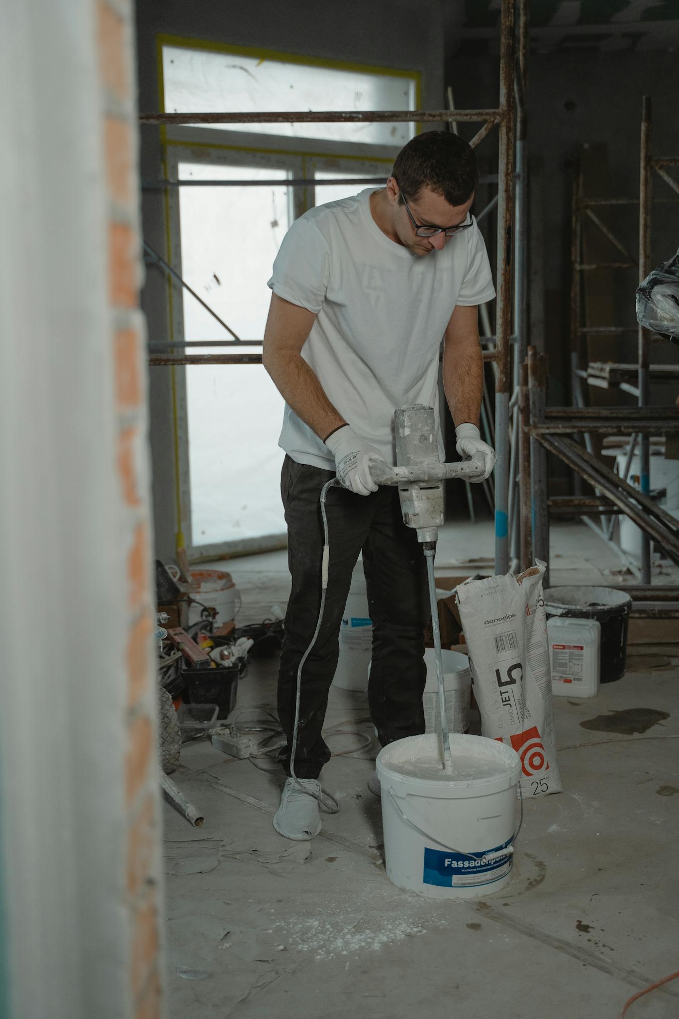 Male construction worker using a mixer to prepare plaster indoors.